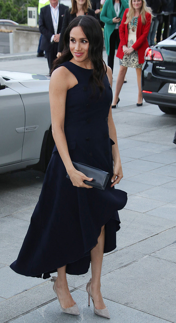 En bild på den brittiska hertiginnan Meghan Markle i en djupt mörkblå klänning och kuvertväska under sin första kungliga utrikesresa.